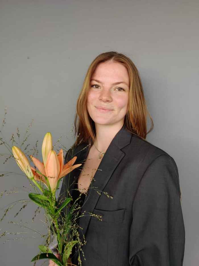 Portrait picture of Antonia Lilja in a grey blazer holding an orange flower